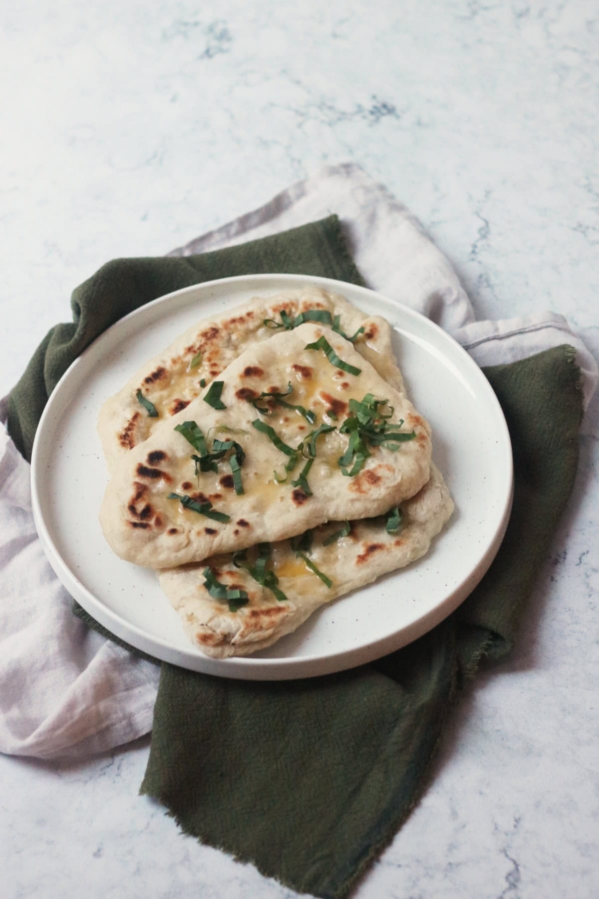 3 Vegan Wild Garlic Naan Breads on a white plate on top of a cream and a green napkin