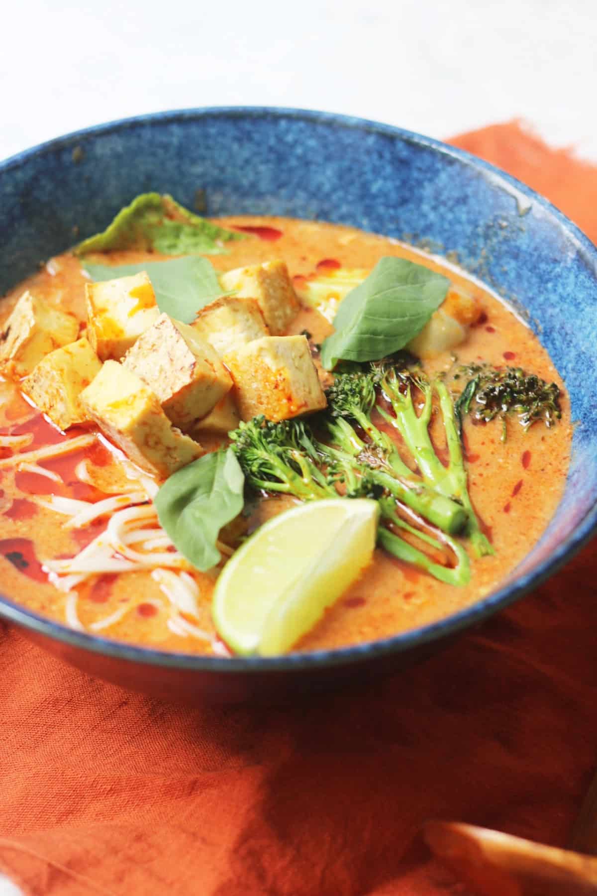 Vegan Thai Red Curry Noodle Soup served in a dark blue ramen bowl with an orange napkin