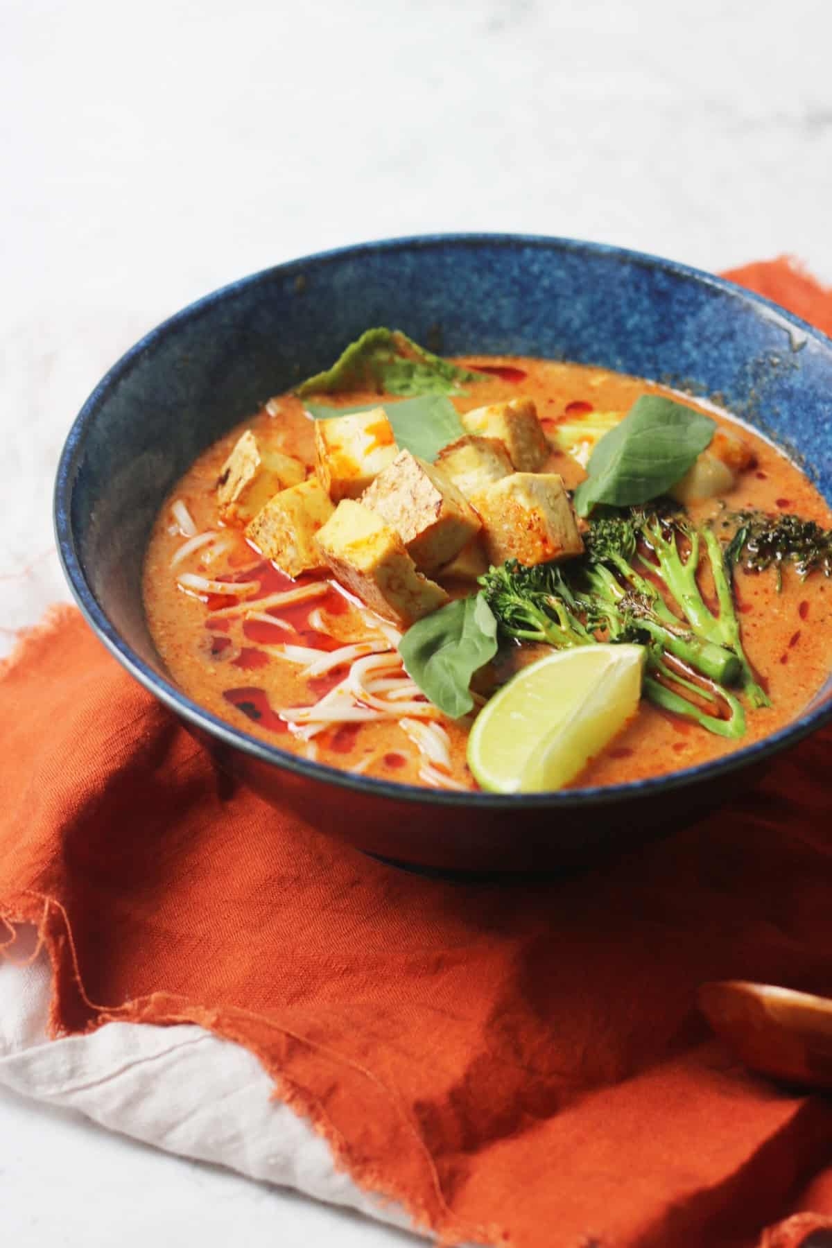 Vegan Thai Red Curry Noodle Soup served in a dark blue ramen bowl with an orange napkin
