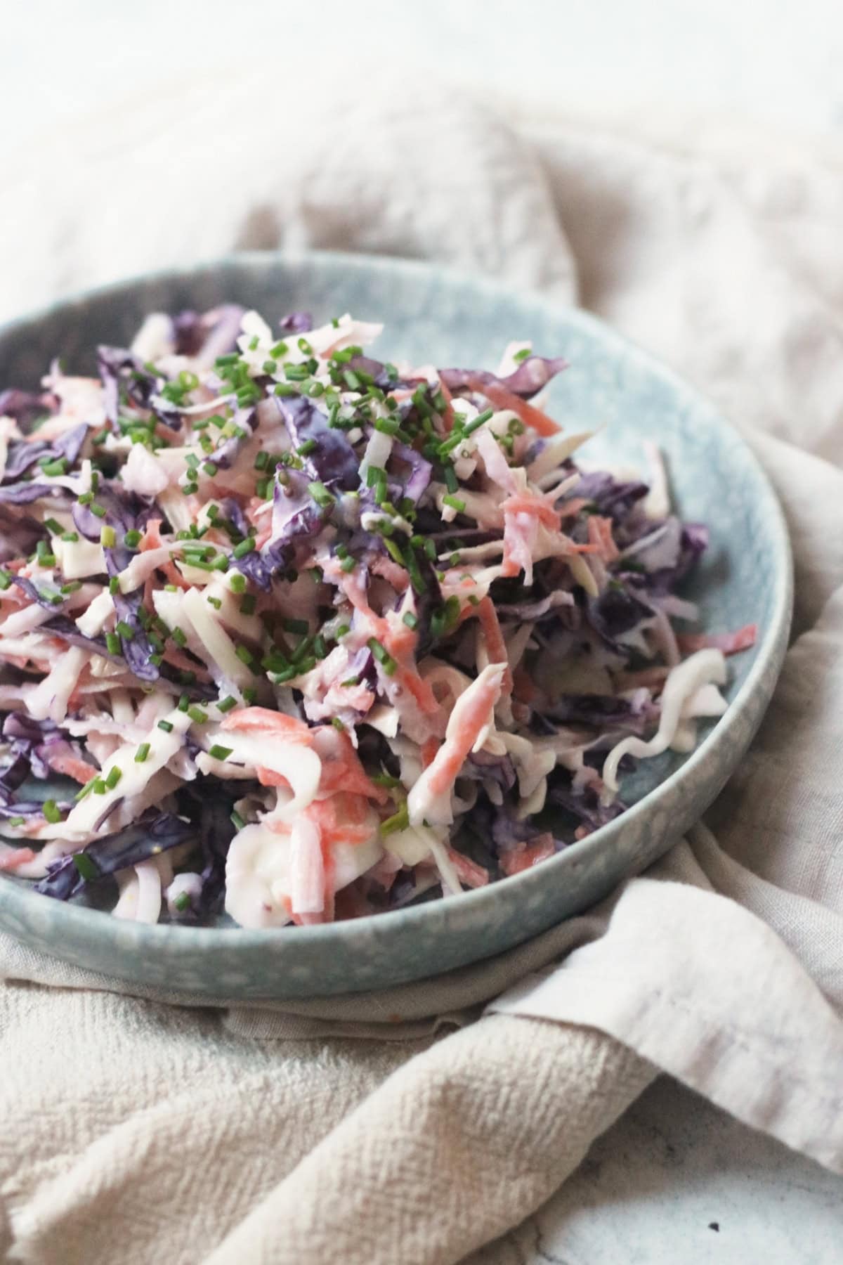 A plate of Vegan Kohlrabi Slaw, topped with chives, served on a light blue plate on top of cream napkins