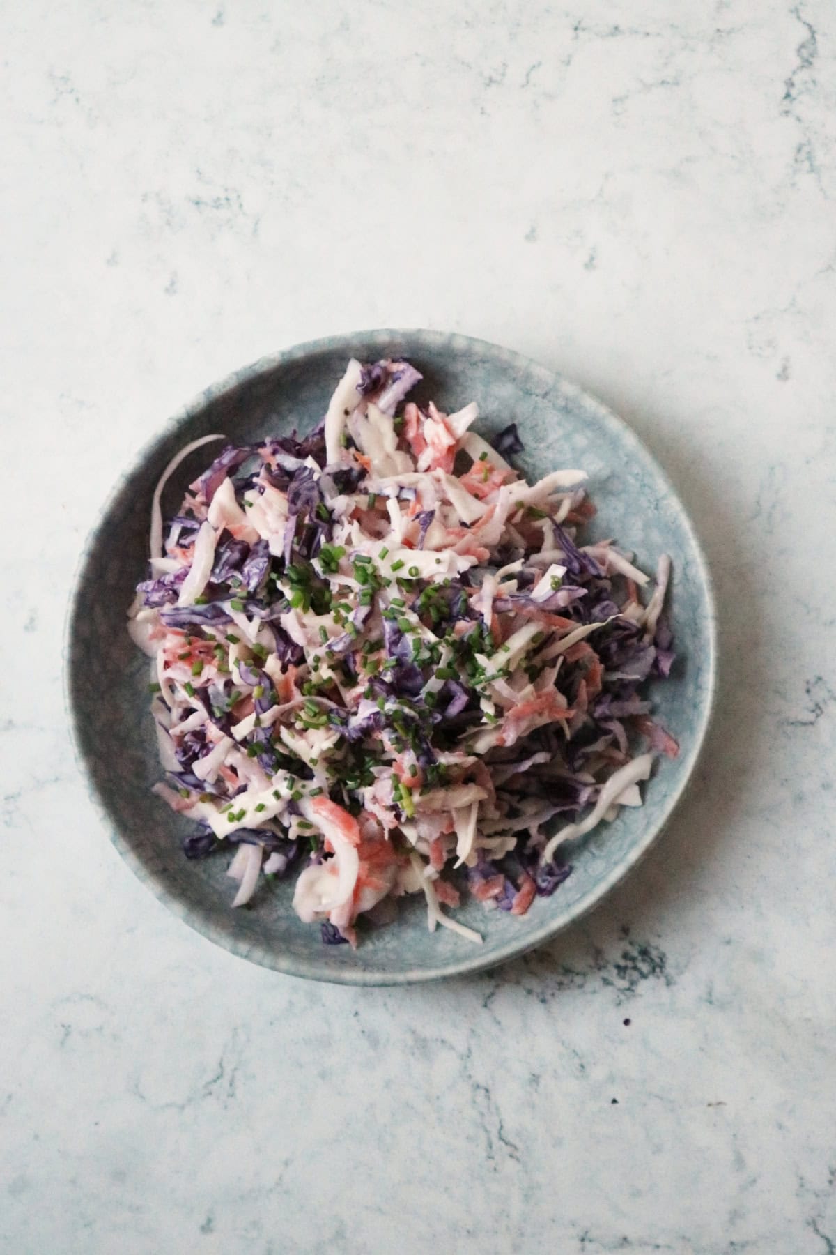 A plate of Vegan Kohlrabi Slaw, topped with chives, served on a light blue plate