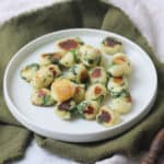 A portion of Vegan Wild Garlic Gnocchi on a white plate that is sat on top of a dark green and cream napkin