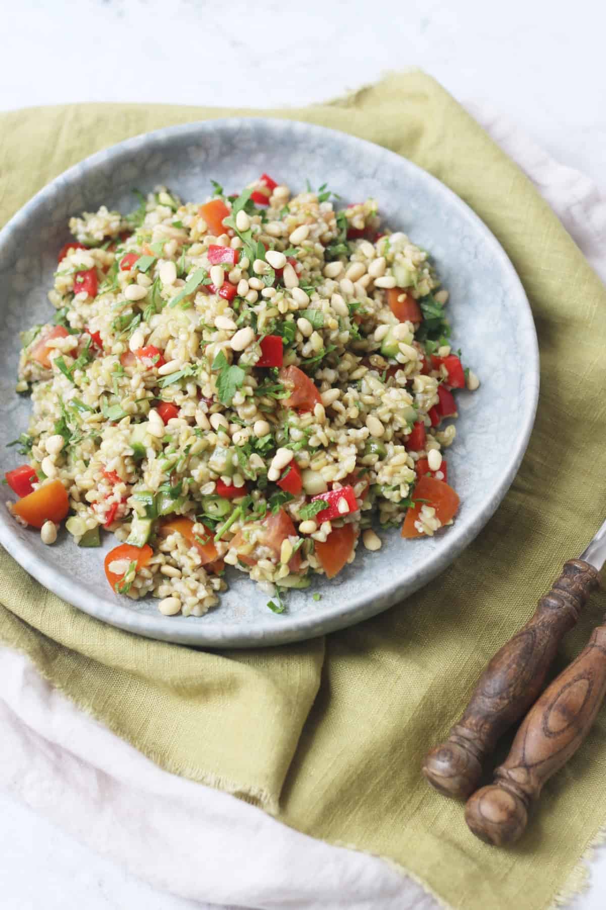 Lemon and Herb Freekeh Salad served on a pale blue plate on top of a green napkin with wooden handled knife and fork