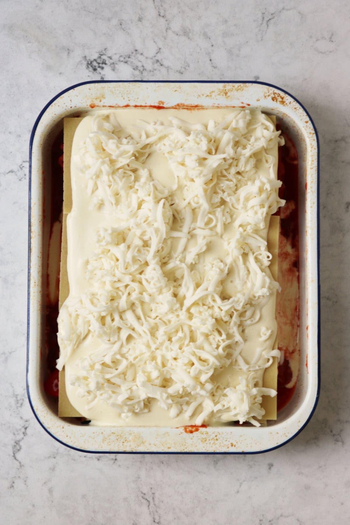 An assembled Vegan Roasted Vegetable Lasagne topped with grated vegan mozzarella ready for the oven.
