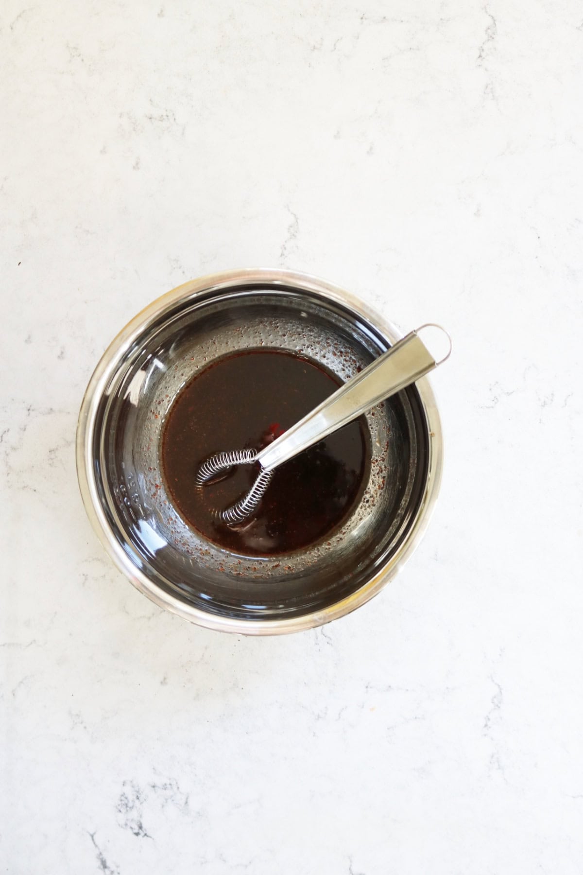 A small metal mixing bowl containing the dressing for Turkish Red Cabbage Salad and a small sauce whisk