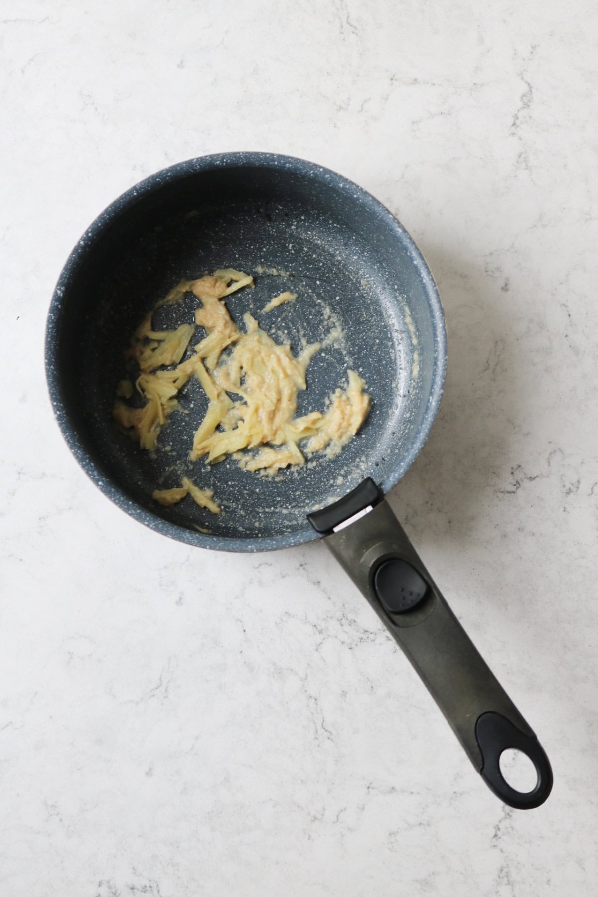 A saucepan with minced garlic and ginger frying gently