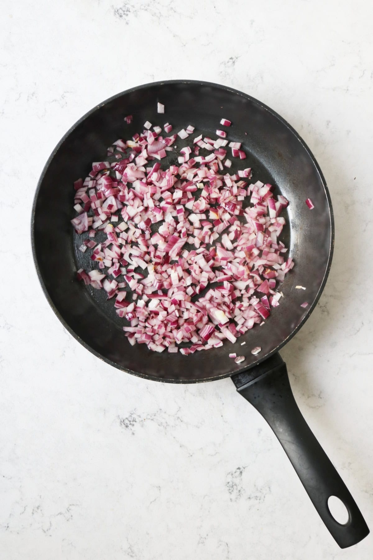 Diced red onion and garlic cooking in a large flat-bottomed sauce pan.