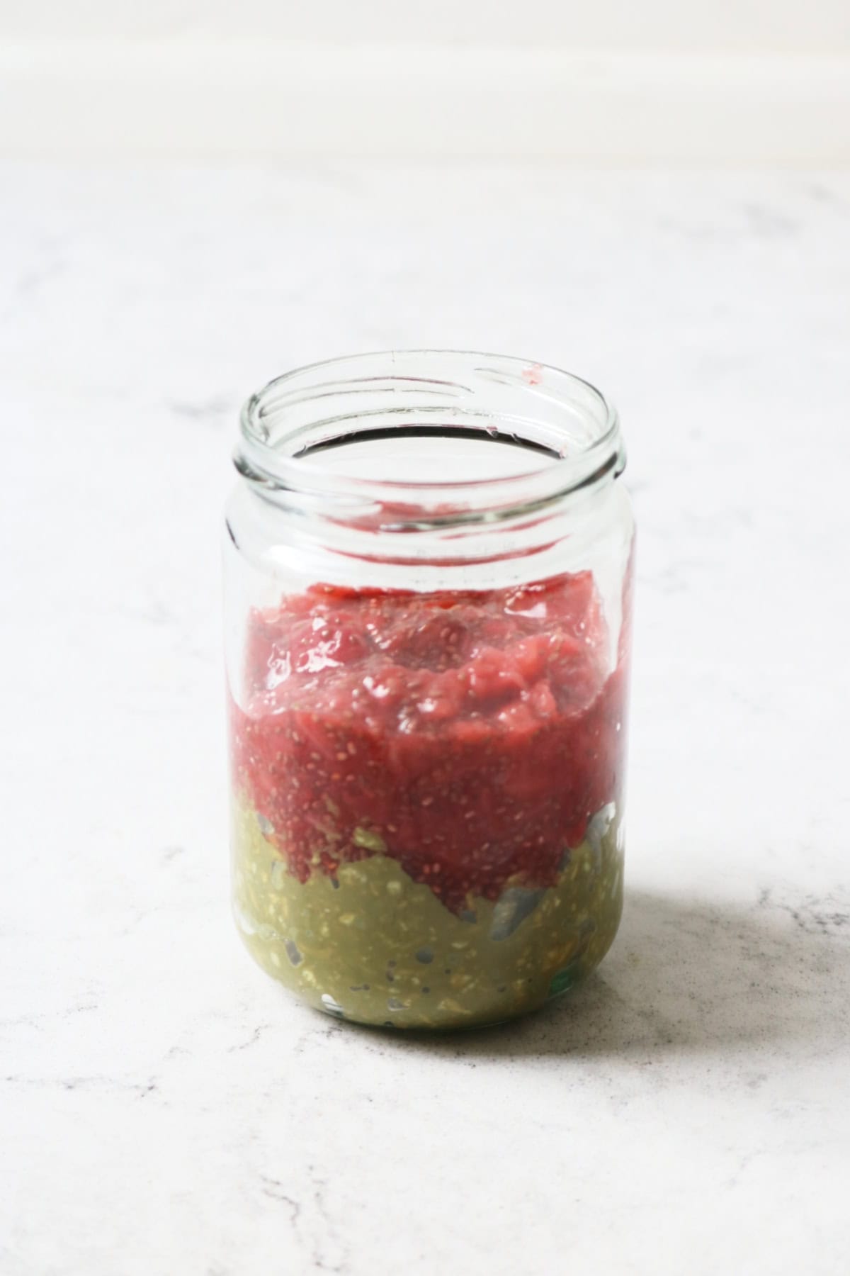 Layers of matcha overnight oats and strawberry chia jam in a glass jar