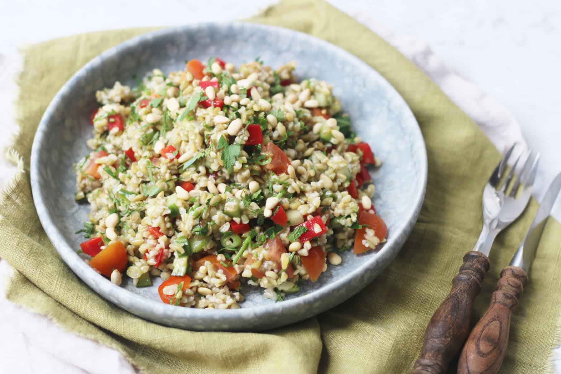 Lemon and Herb Freekeh Salad served on a pale blue plate on top of a green napkin with wooden handled knife and fork