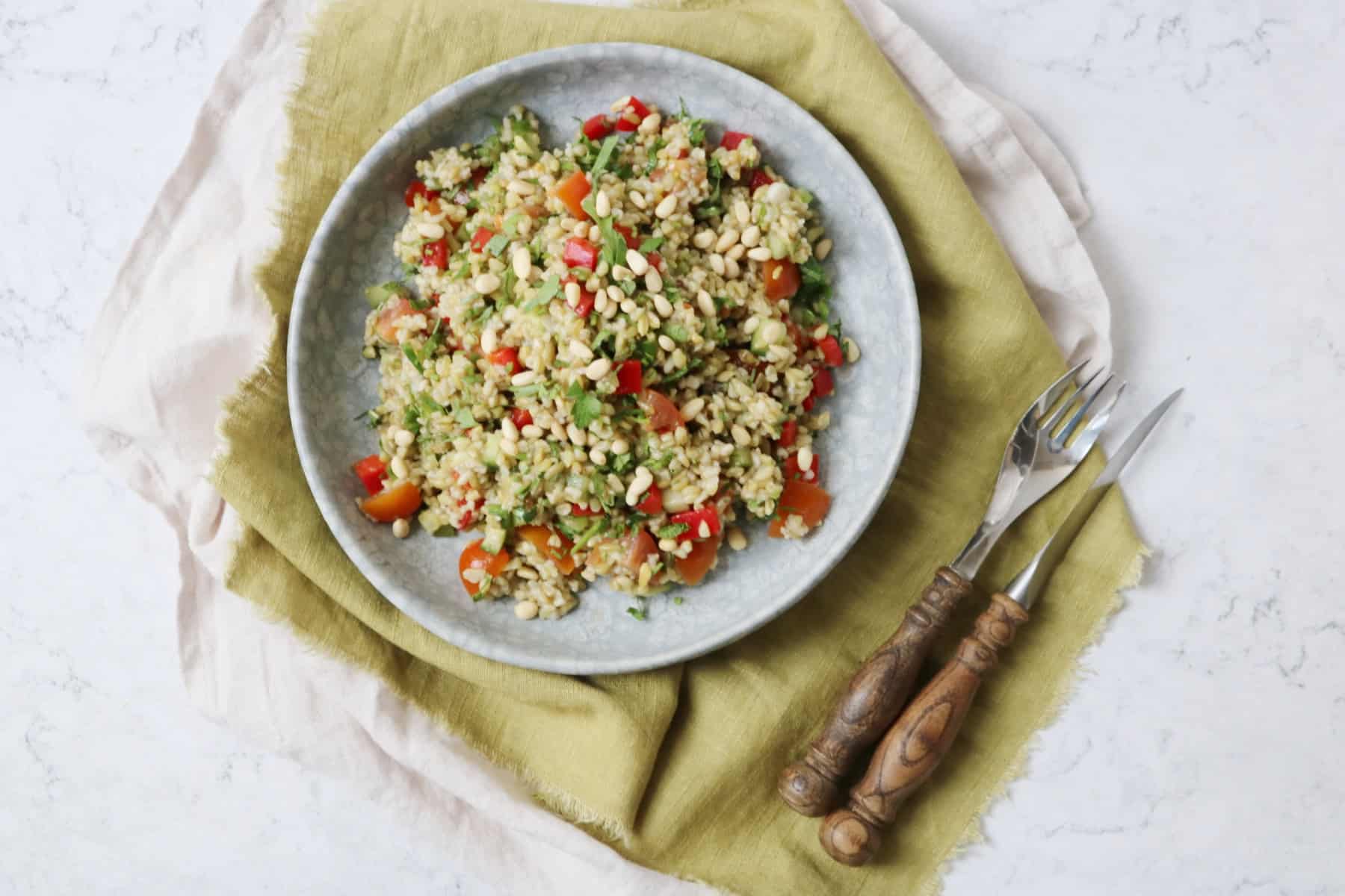 Lemon and Herb Freekeh Salad served on a pale blue plate on top of a green napkin with wooden handled knife and fork