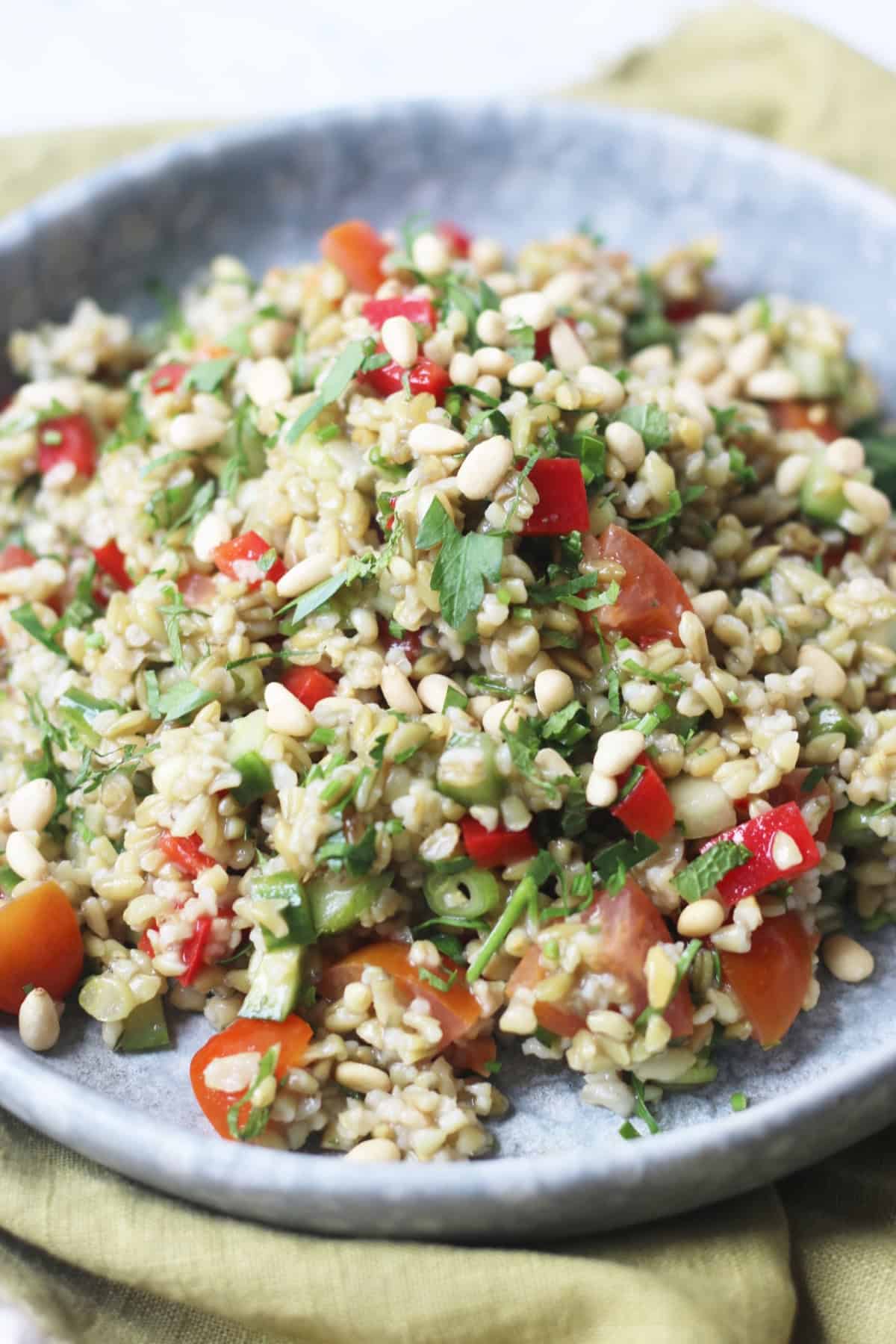 Lemon and Herb Freekeh Salad served on a pale blue plate on top of a green napkin with wooden handled knife and fork