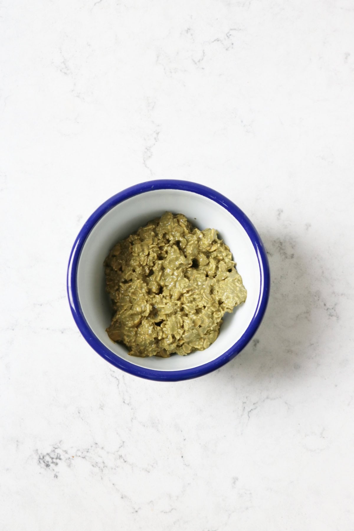 Matcha overnight oats mixed in a white and blue enamel bowl on a white marble countertop