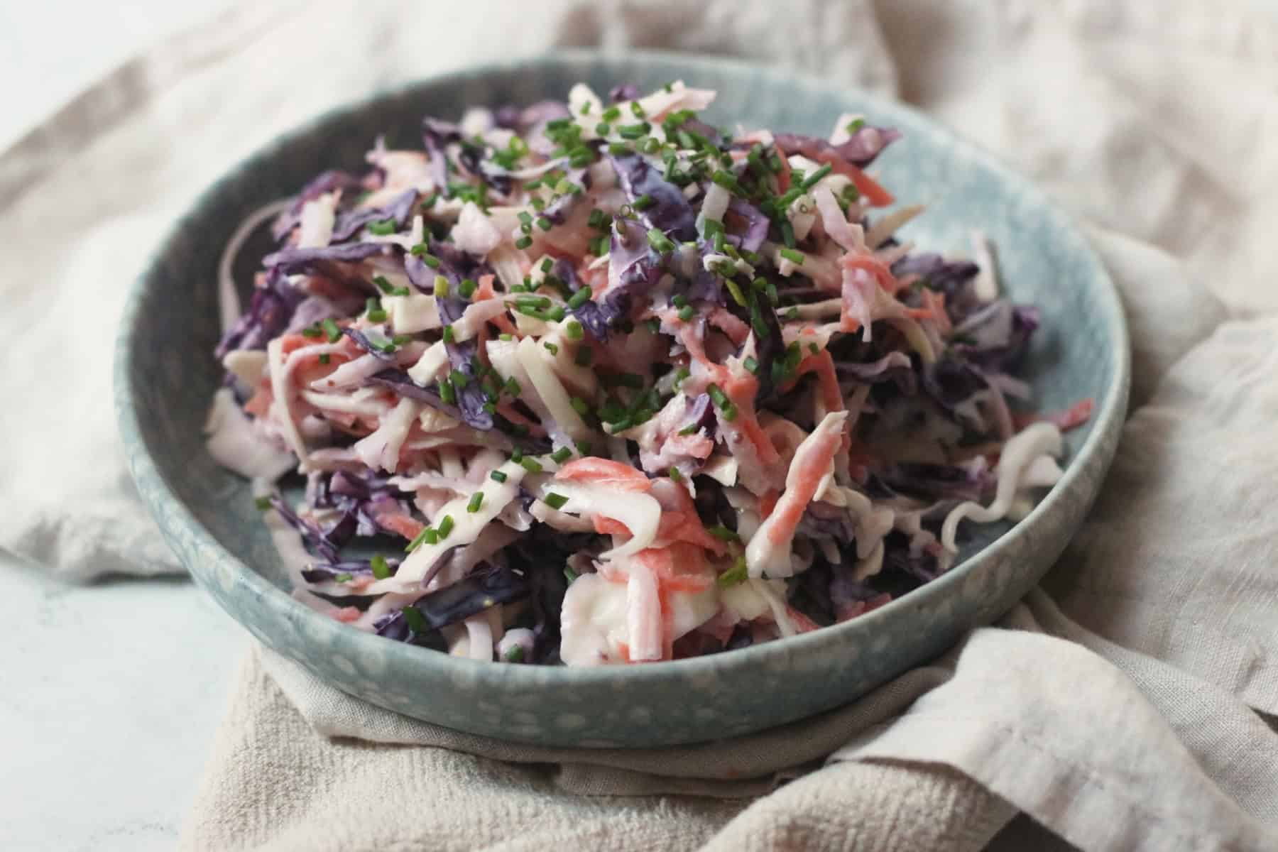 A plate of Vegan Kohlrabi Slaw, topped with chives, served on a light blue plate on top of cream napkins