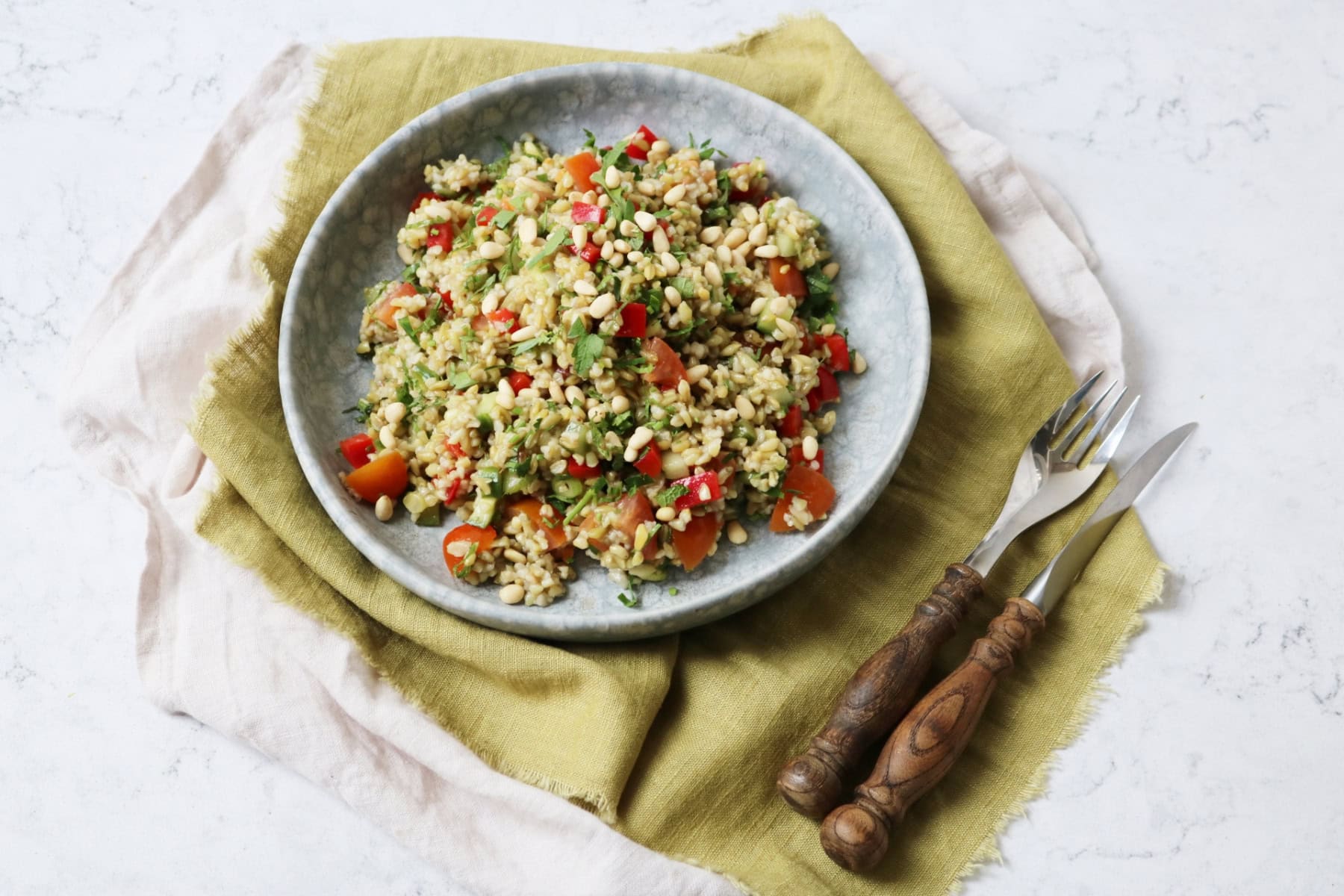 Lemon and Herb Freekeh Salad served on a pale blue plate on top of a green napkin with wooden handled knife and fork