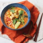 Vegan Thai Red Curry Noodle Soup served in a dark blue ramen bowl with an orange napkin and wood spoons and chopsticks