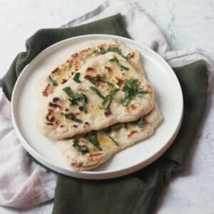 3 Vegan Wild Garlic Naan Breads on a white plate on top of a cream and a green napkin