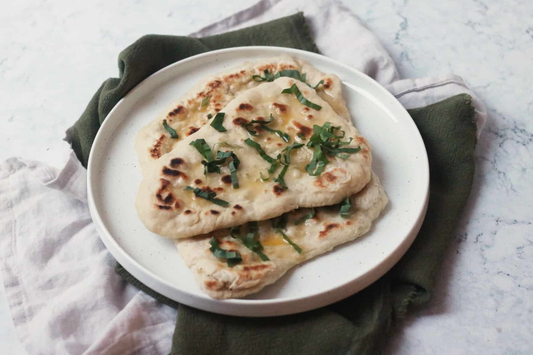 3 Vegan Wild Garlic Naan Breads on a white plate on top of a cream and a green napkin