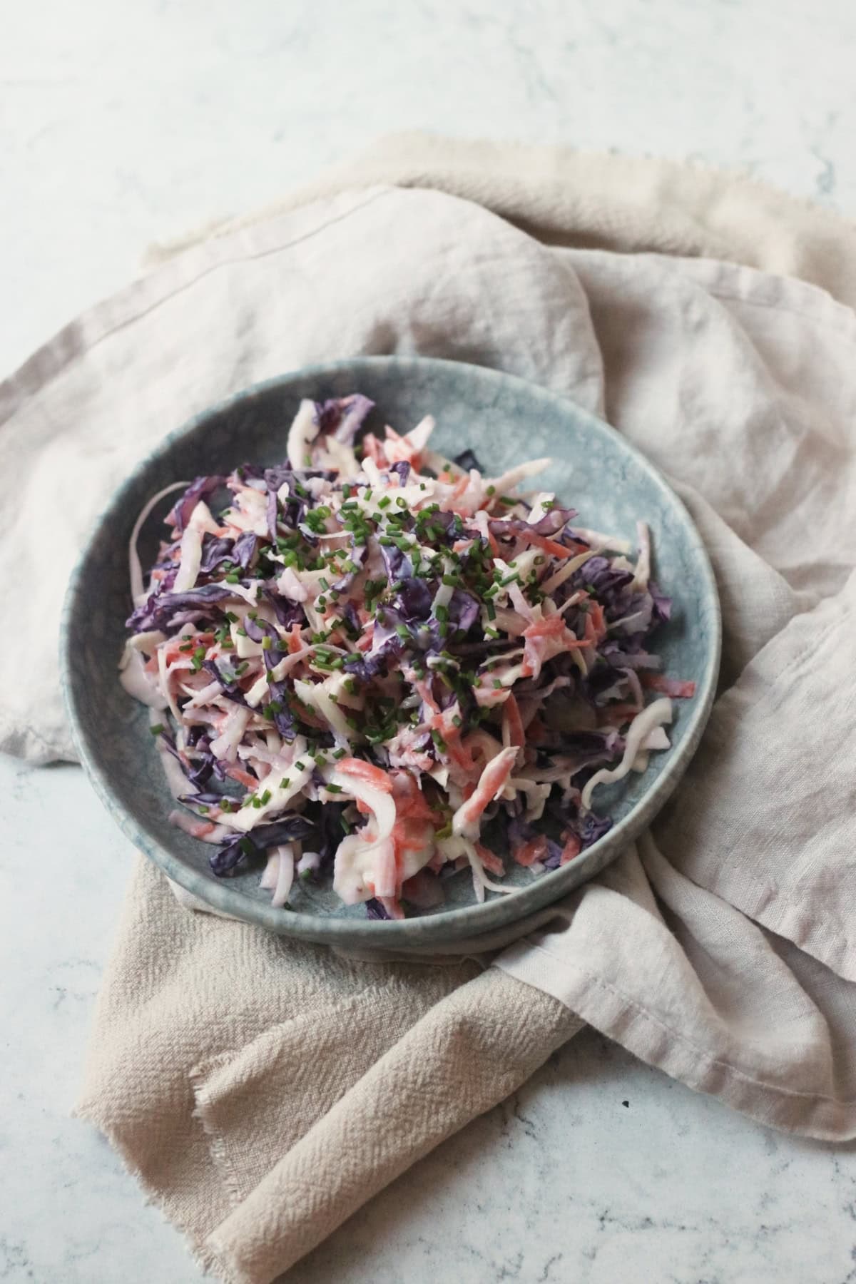 A plate of Vegan Kohlrabi Slaw, topped with chives, served on a light blue plate on top of cream napkins