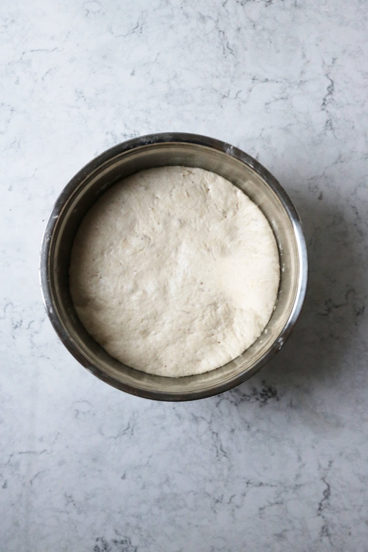 A large metal mixing bowl filled with dough for vegan naan breads which has puffed up near to the top of the bowl