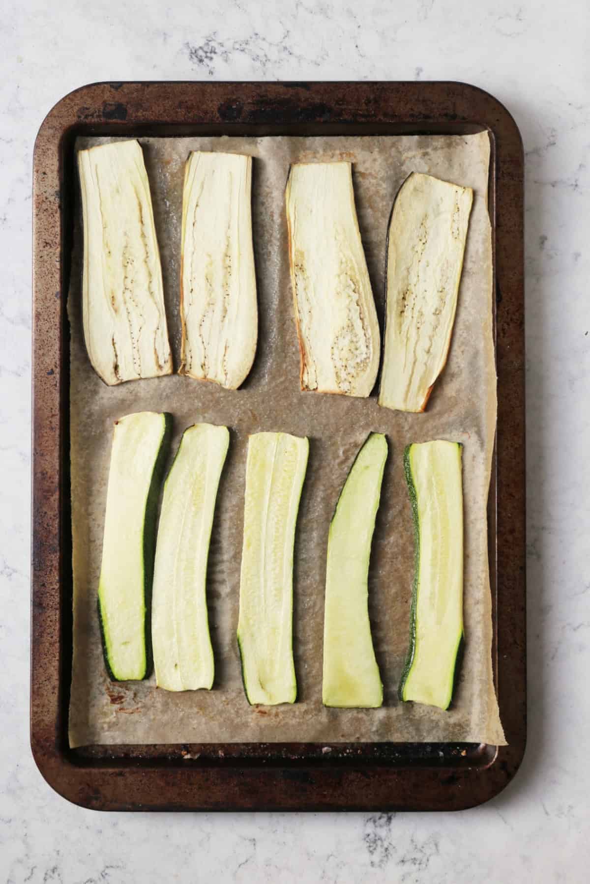 Strips of roasted aubergine and courgette on a baking tray.