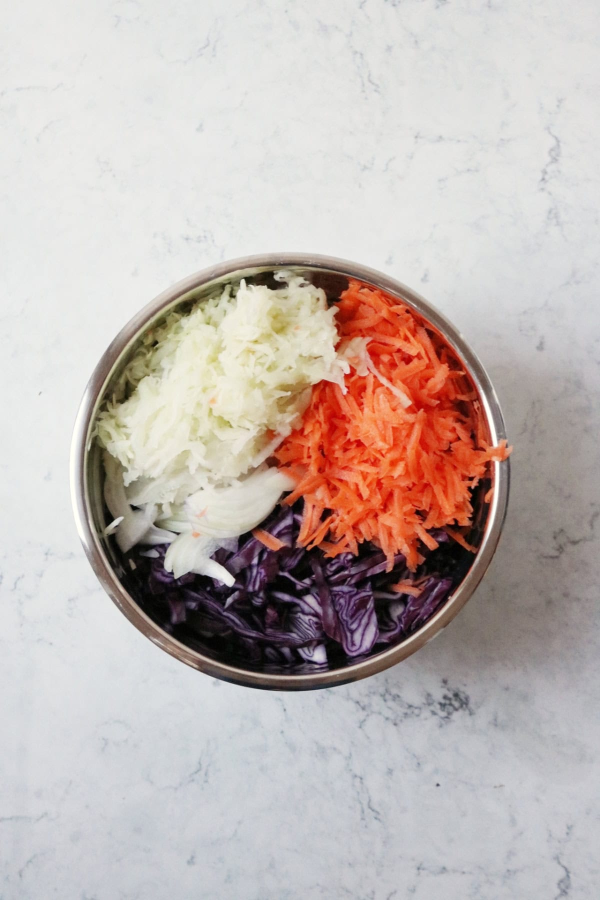 A large metal mixing bowl filled with shredded cabbage, carrot, white onion and kohlrabi