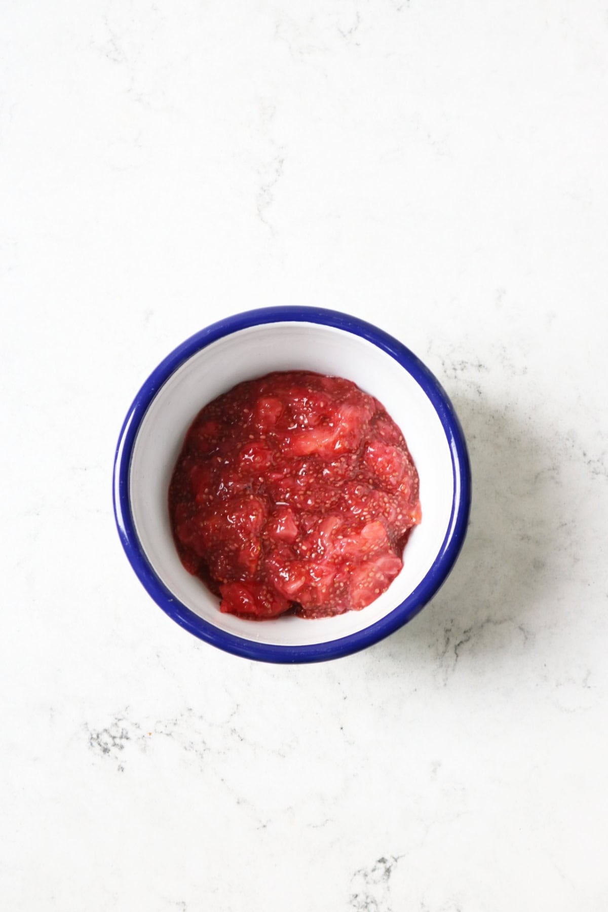 Strawberry chia seed jam mixed in a white and blue enamel bowl on a white marble countertop