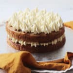 A Vegan Banana Cake with Vegan Cream Cheese Frosting on a silver cake board sat on top of yellow and cream napkins