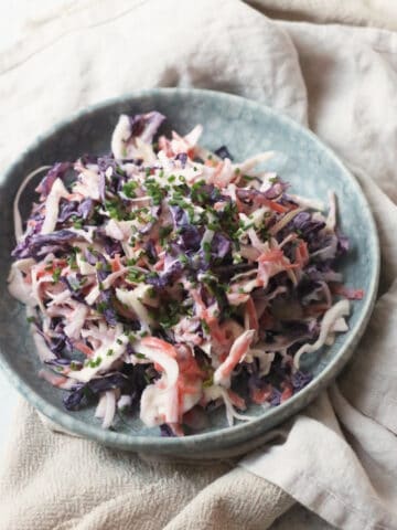 A plate of Vegan Kohlrabi Slaw, topped with chives, served on a light blue plate on top of cream napkins