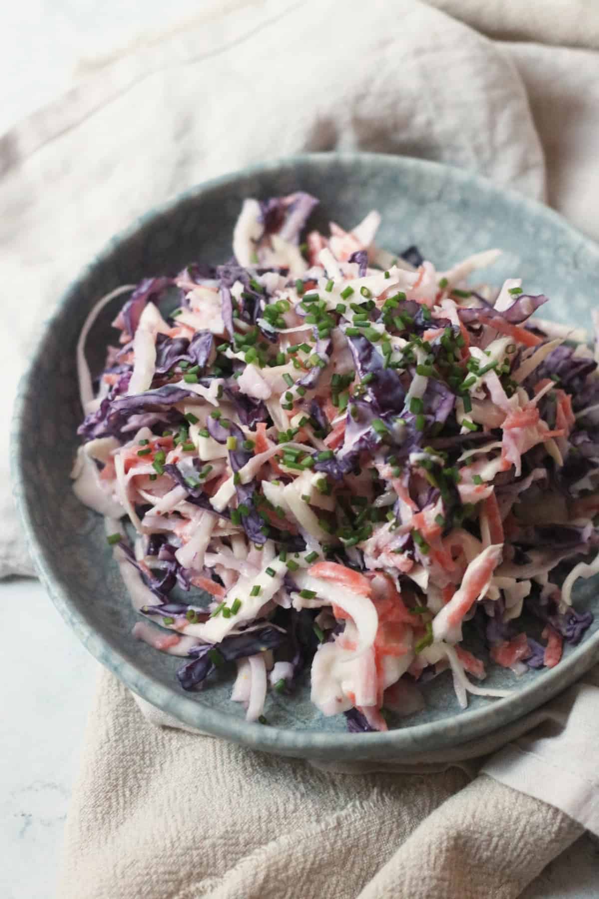 A plate of Vegan Kohlrabi Slaw, topped with chives, served on a light blue plate on top of cream napkins