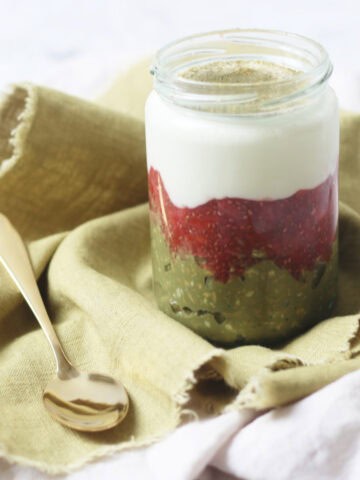 A jar of Vegan Strawberry and Matcha Overnight Oats on a green napkin with a gold teaspoon