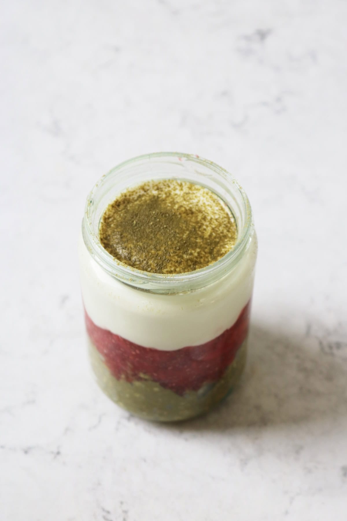 A jar of Vegan Strawberry and Matcha Overnight Oats made up of layers of oats, jam and yogurt, dusted with matcha