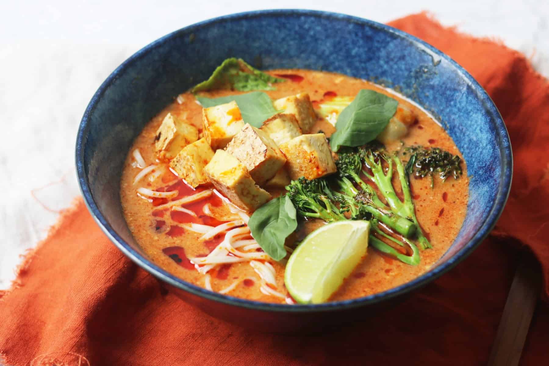 Vegan Thai Red Curry Noodle Soup served in a dark blue ramen bowl with an orange napkin