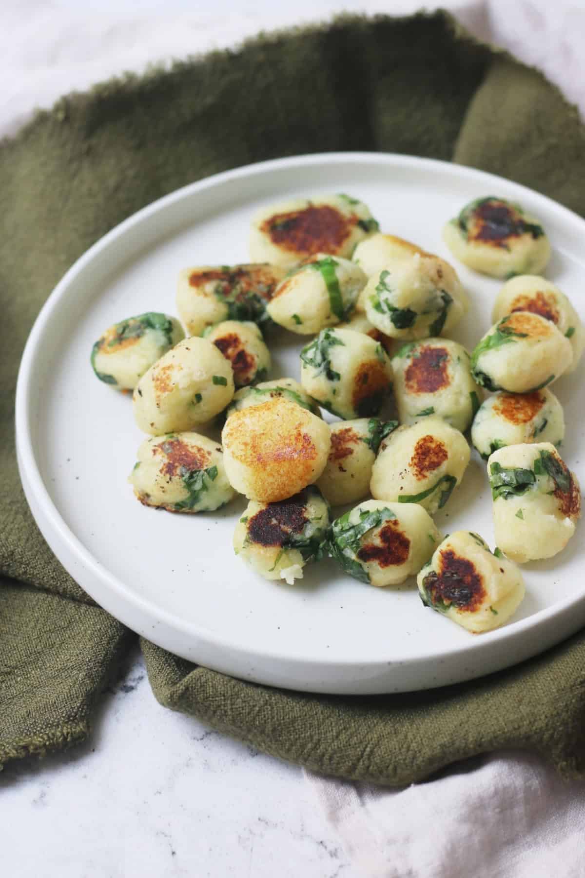 A portion of Vegan Wild Garlic Gnocchi on a white plate that is sat on top of a dark green and cream napkin