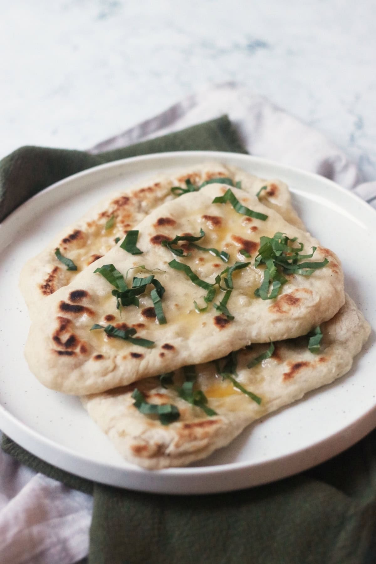 3 Vegan Wild Garlic Naan Breads on a white plate on top of a cream and a green napkin