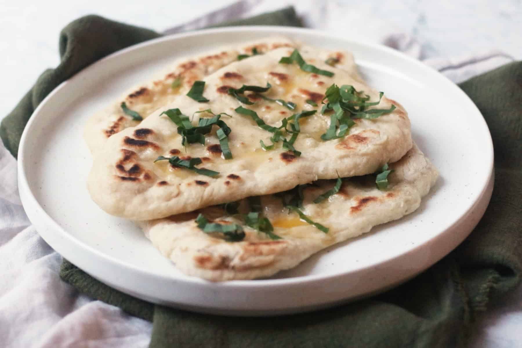3 Vegan Wild Garlic Naan Breads on a white plate on top of a cream and a green napkin