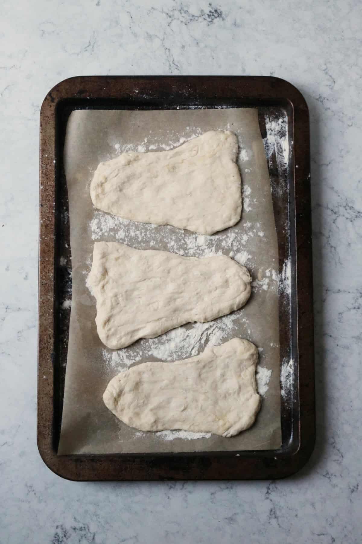 3 uncooked vegan naan breads laid out on a baking tray