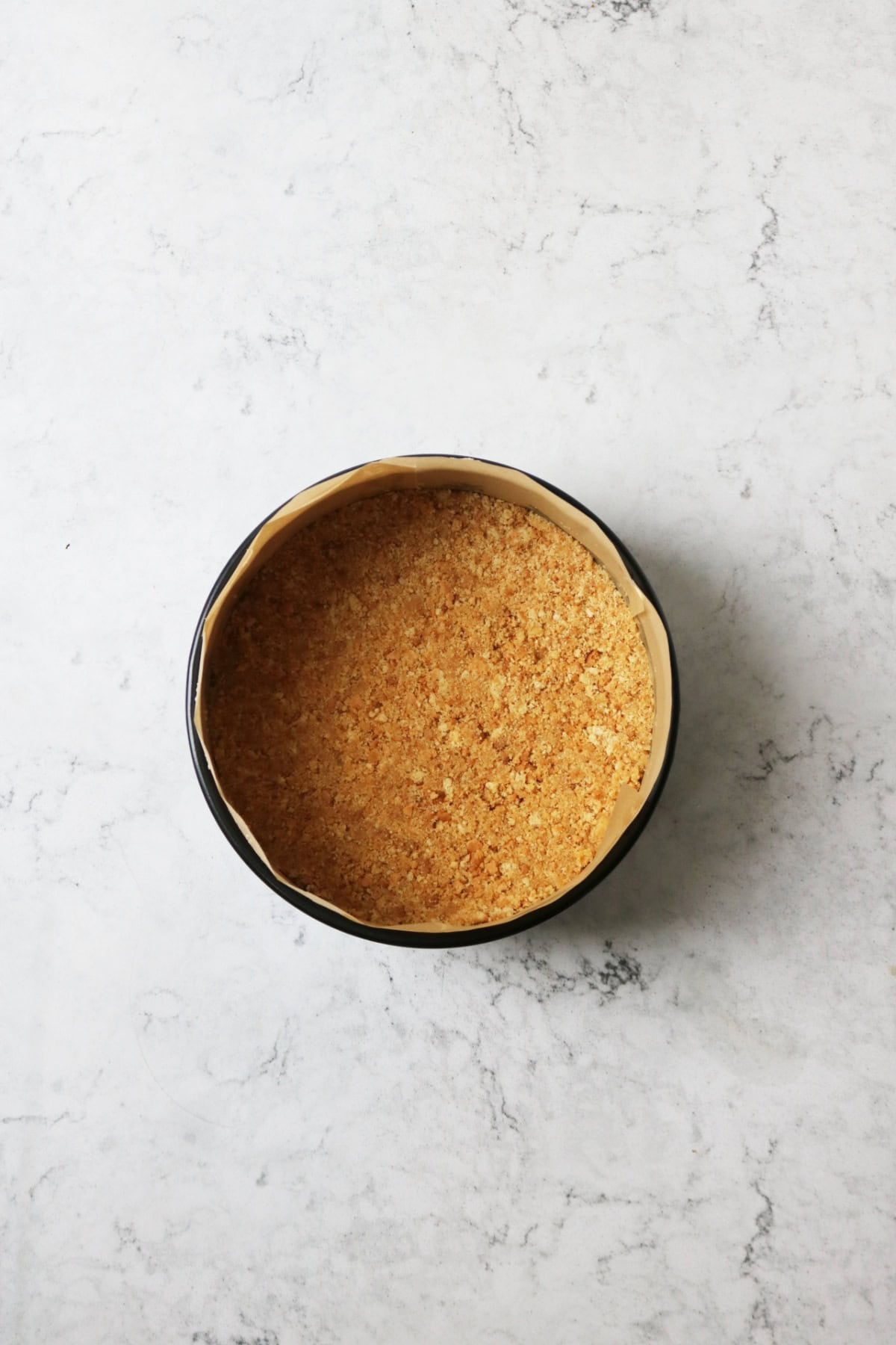 Buttery biscuit crumbs pressed into the bottom of a cake tin to form the base of a vegan cheesecake