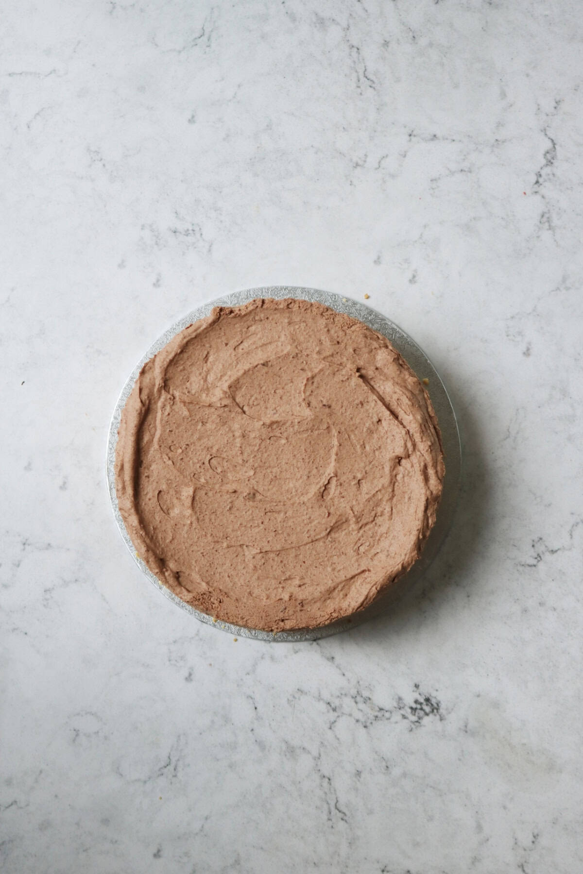 An aerial view of the top of a vegan chocolate cheesecake on a white marble counter top