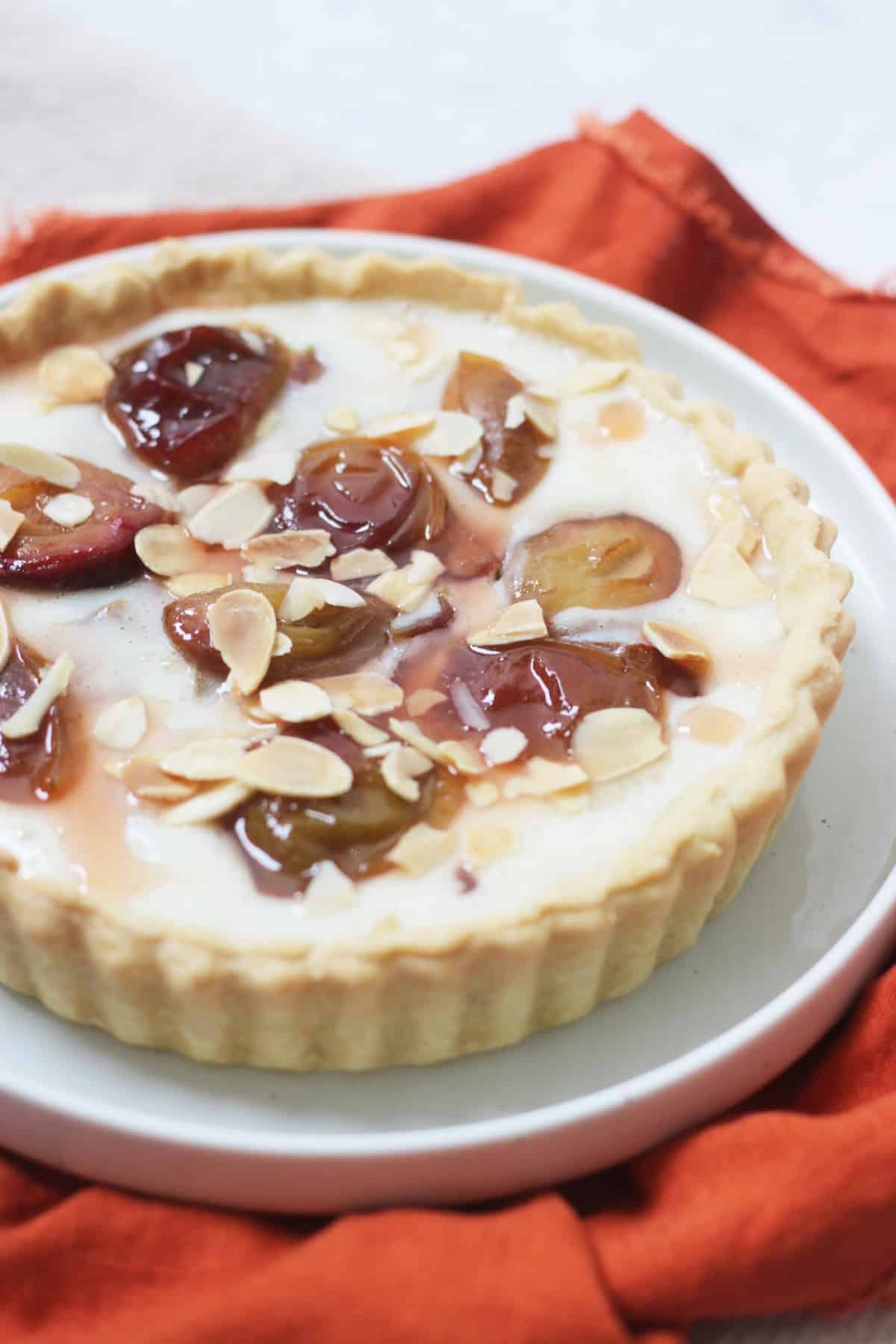 A vegan plum and custard tart topped with toasted flaked almonds.