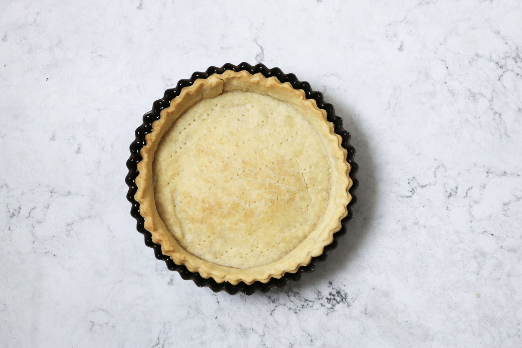 A circular shortcrust pastry tart case cooling while still in the tin.