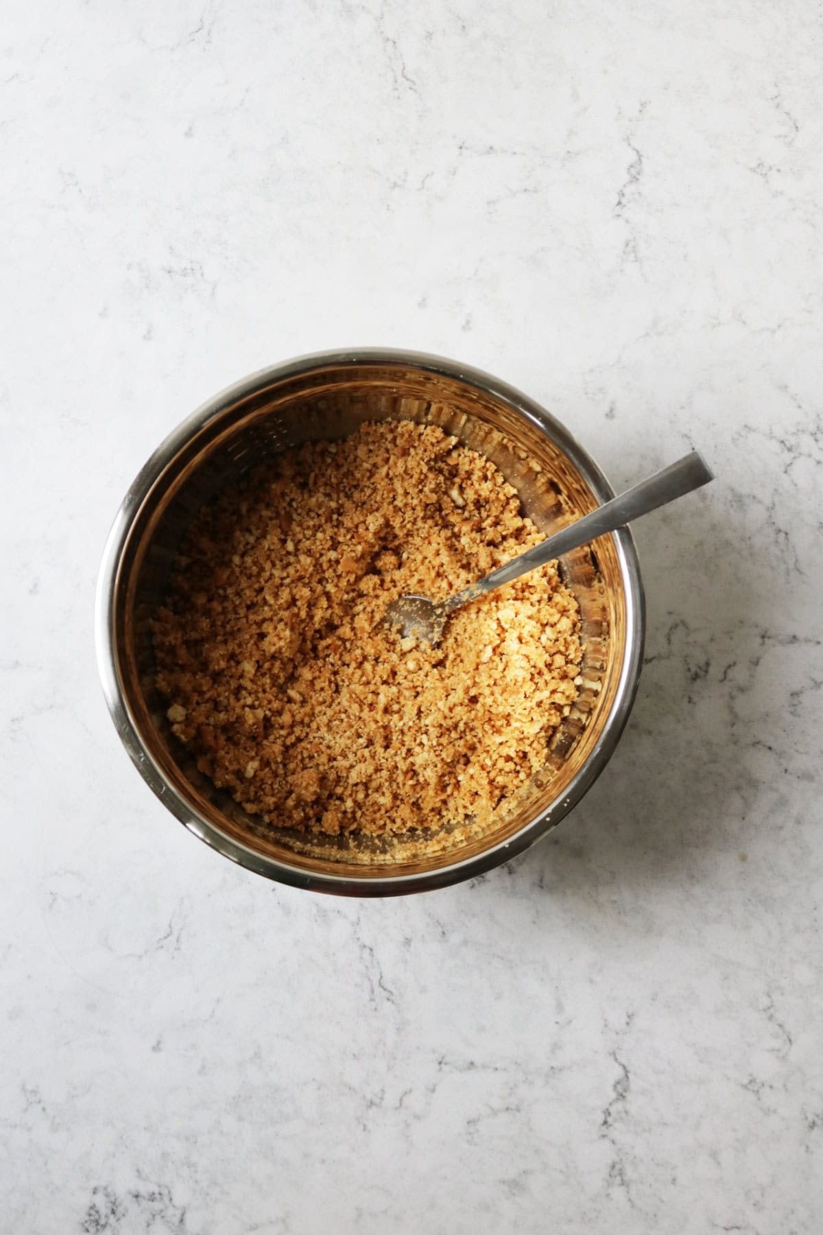 A metal mixing bowl filled with crushed biscuit crumbs and melted butter