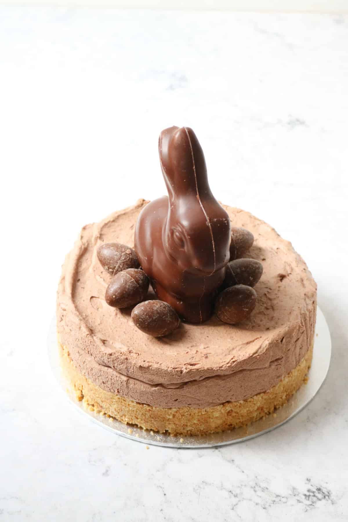 A Vegan Chocolate Cheesecake decorated with a chocolate bunny rabbit and small chocolate eggs sat on top of a silver cake board