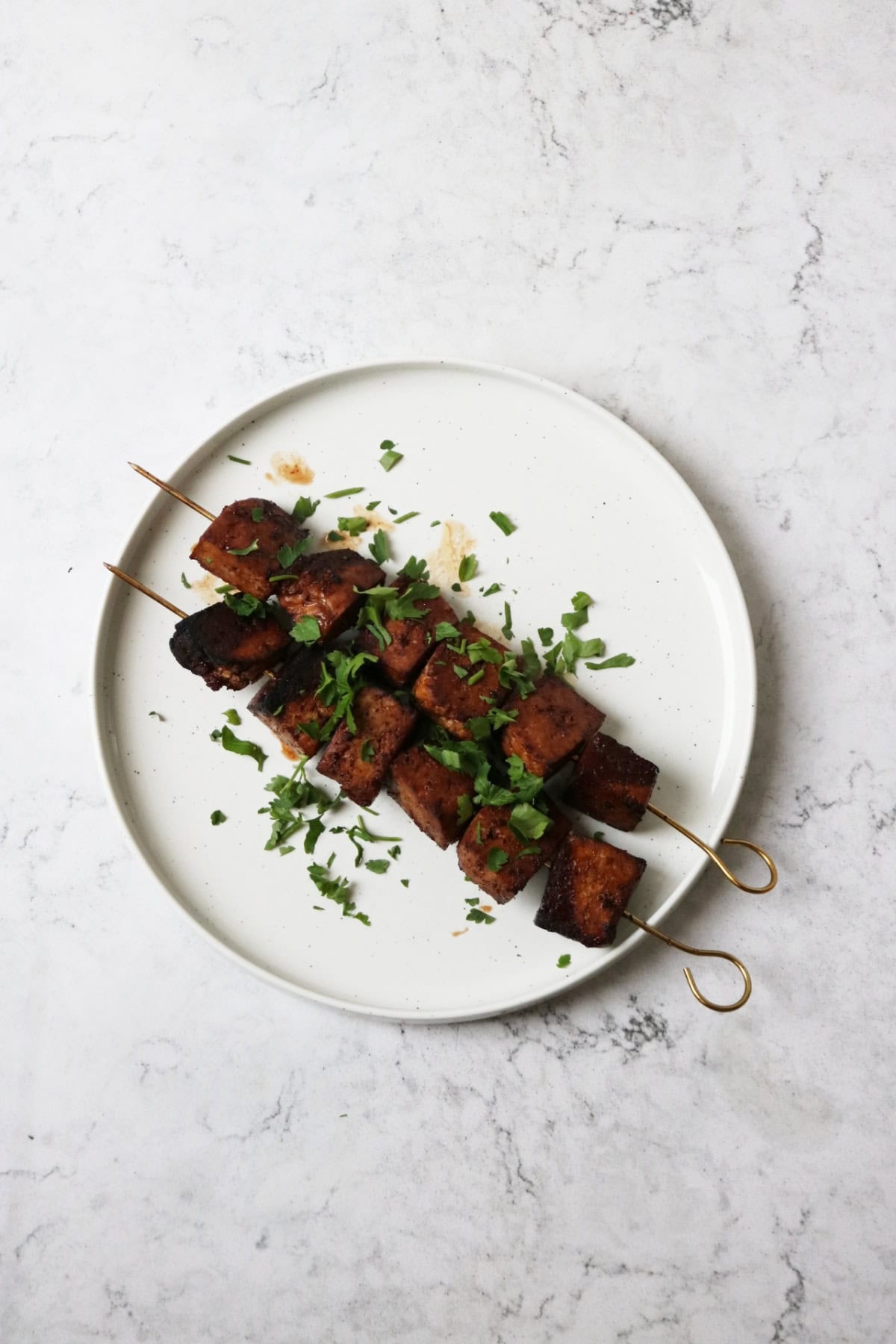 Grilled Pomegranate Molasses Tofu Kebabs served on a white plate with a scattering of fresh herbs
