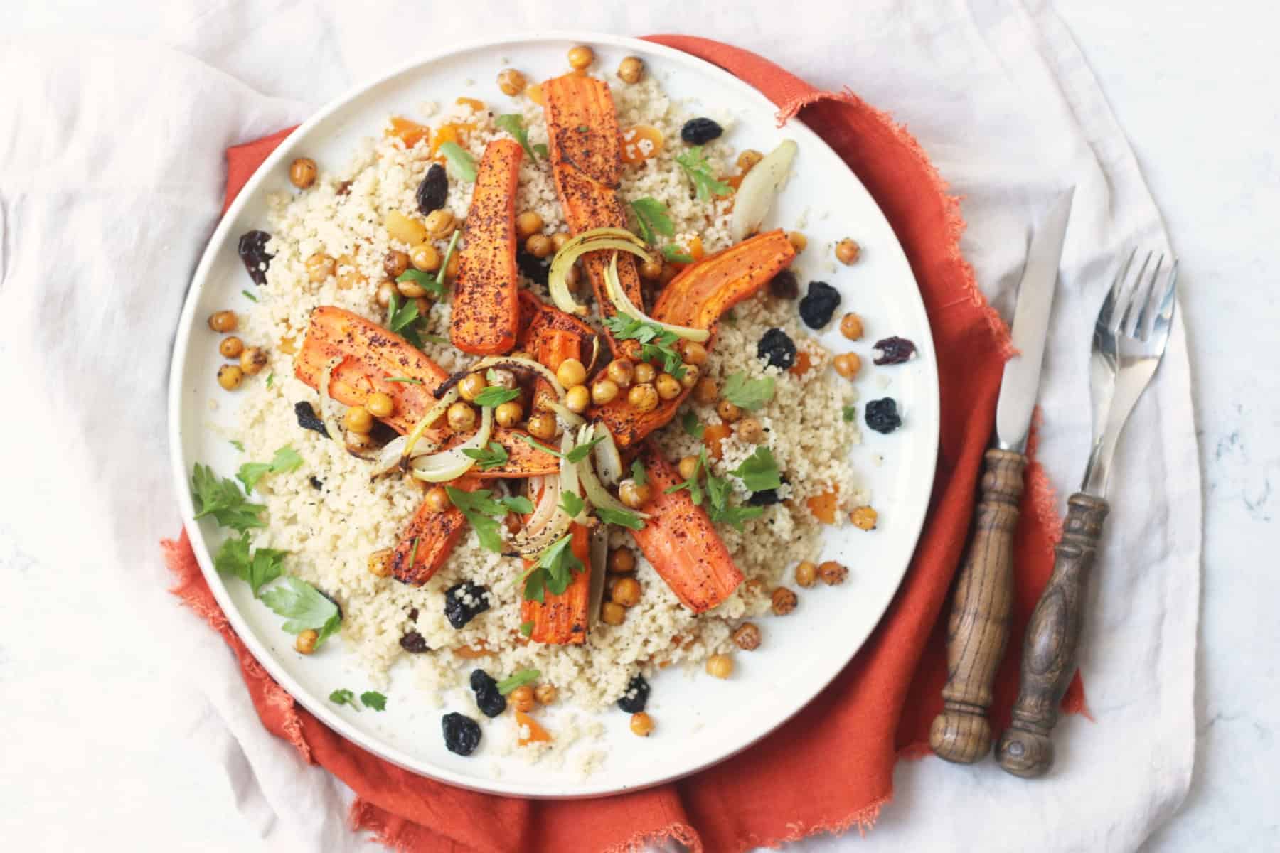 Vegan Warm Moroccan Spiced Couscous with Roasted Carrots on a white plate on top of an orange napkin