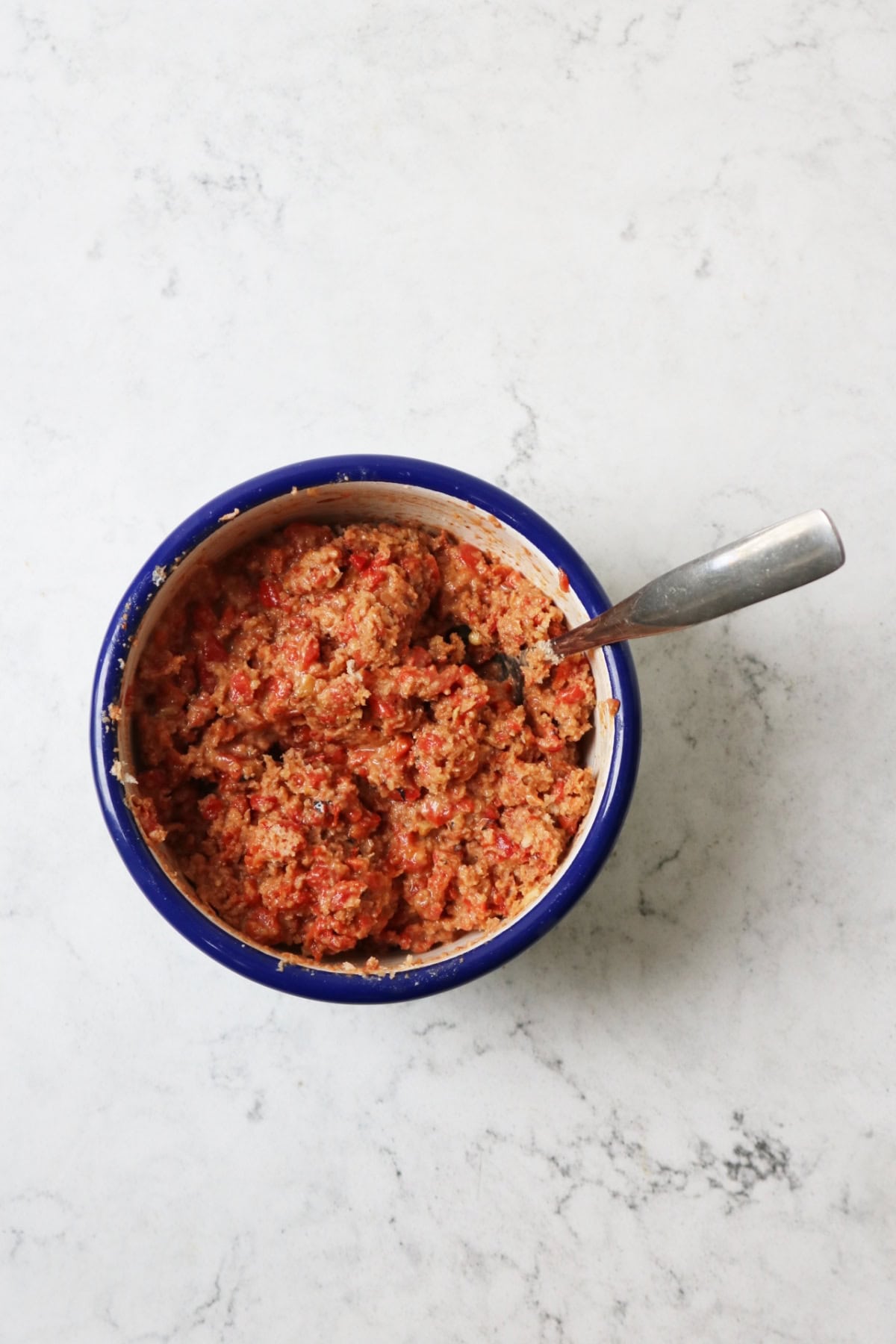 Muhammara in an enamel mixing bowl with a dark blue rim with a silver spoon