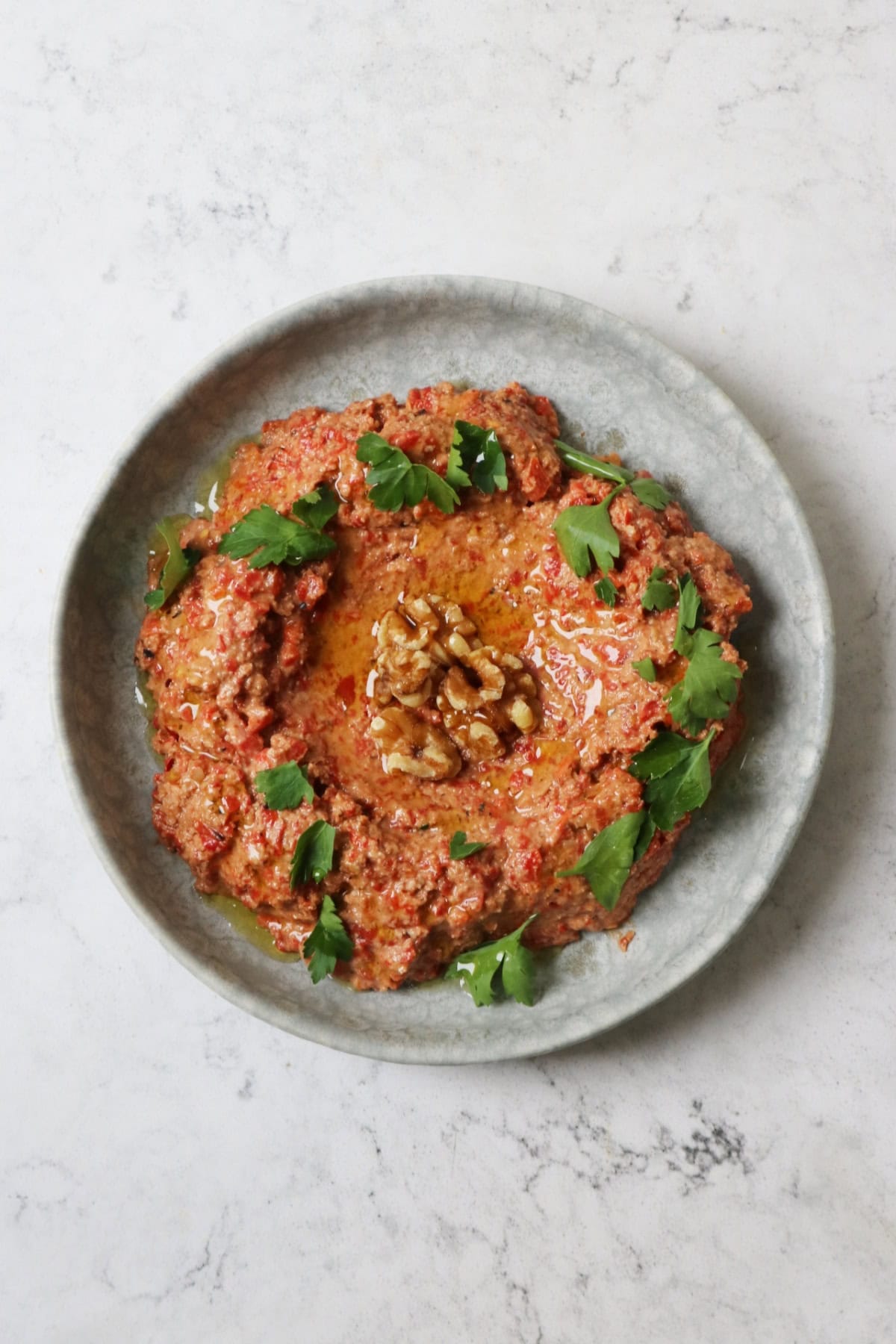 Muhammara, a roasted red pepper and walnut dip served with walnut halves and parsley on a pale blue plate