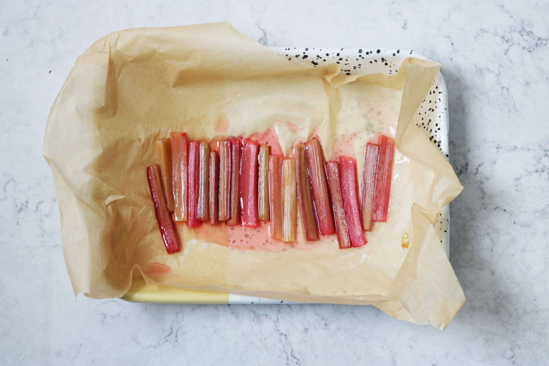 Batons of roasted rhubarb cooling in an oven dish lined with brown baking paper