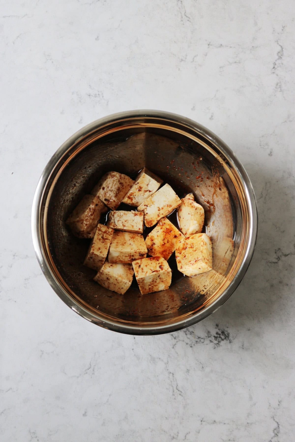 Cubes of tofu in a metal mixing bowl with a marinade made from pomegranate molasses