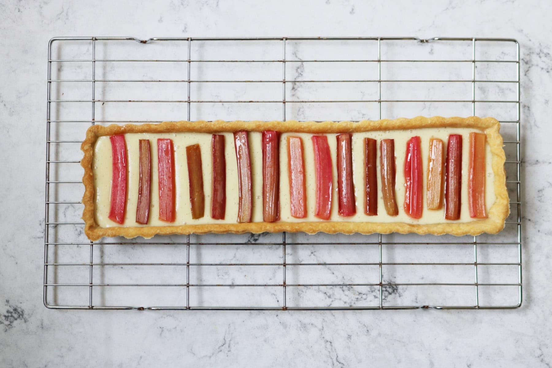 A fully set Vegan Rhubarb and Custard Tart on a wire rack