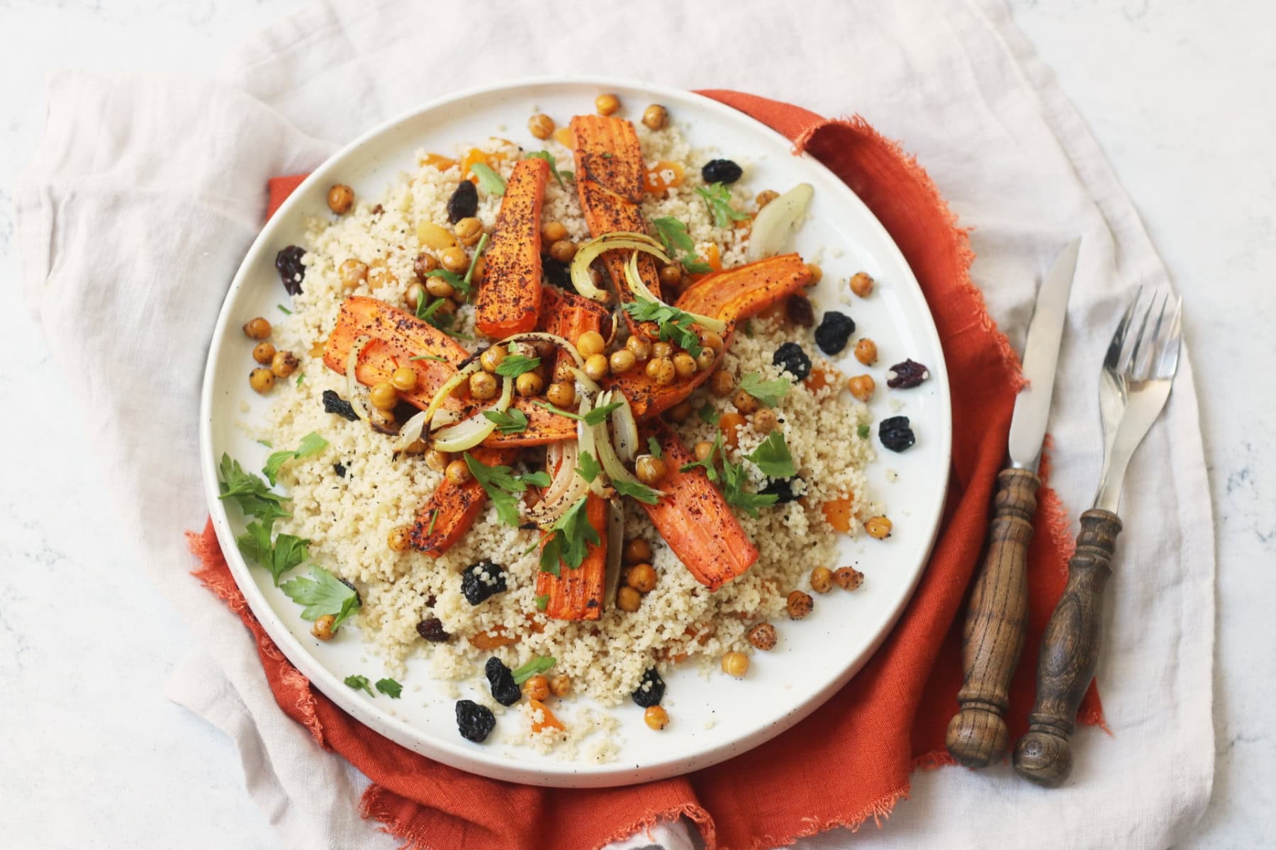 Vegan Warm Moroccan Spiced Couscous with Roasted Carrots on a white plate on top of an orange napkin